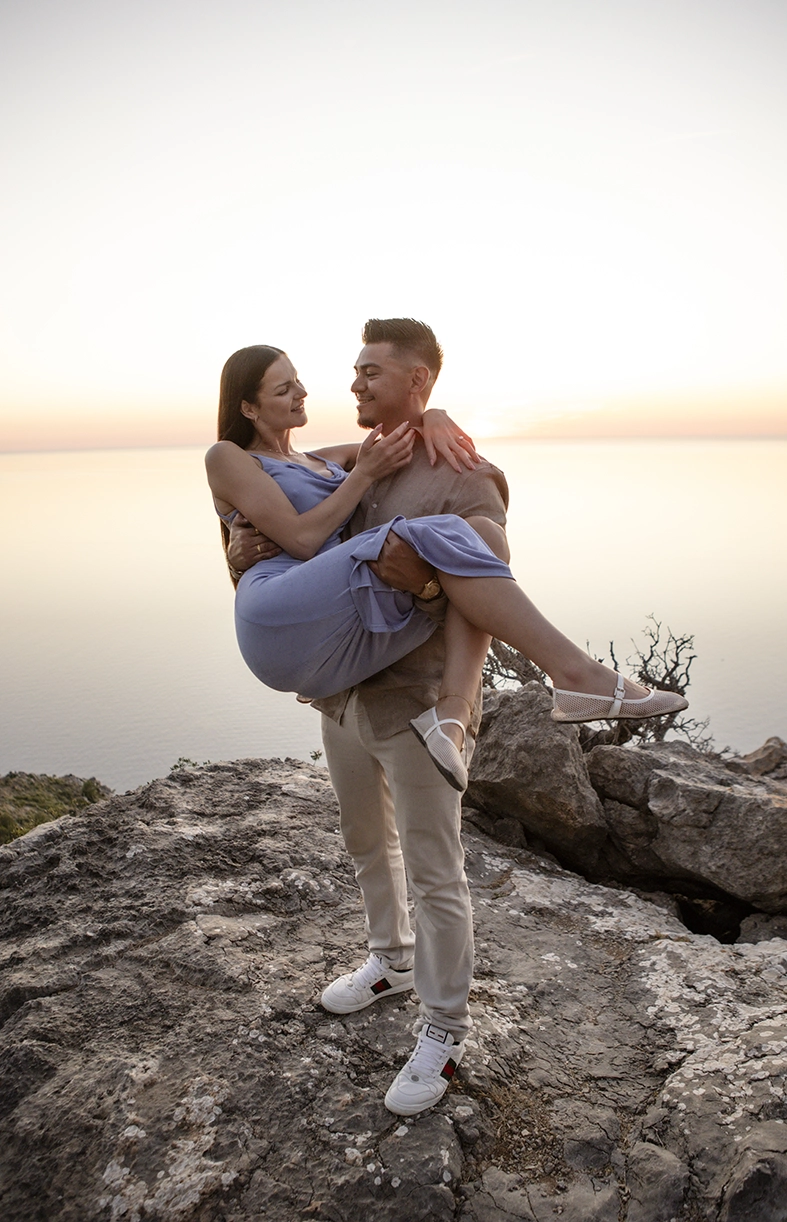 David carries Katie in his arms on the cliffs during a romantic sunset couple session in Mallorca.