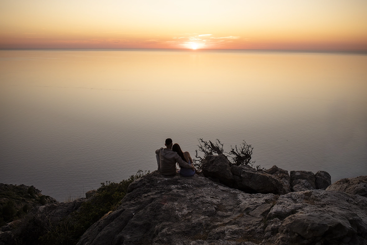Katie and David sit together watching a breathtaking Mediterranean sunset after their engagement in Mallorca.