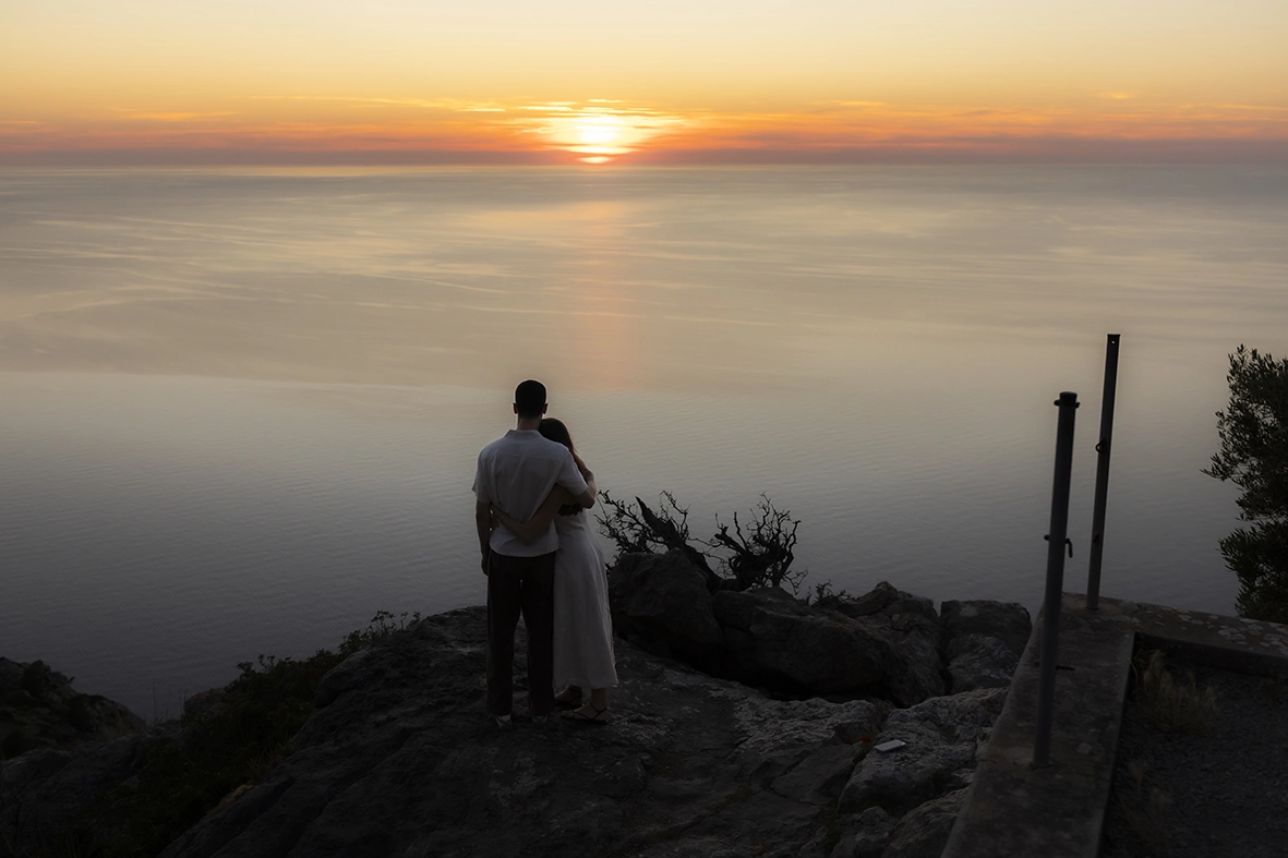 Engaged couple watching the sunset after a proposal photographed by an engagement photographer in Mallorca