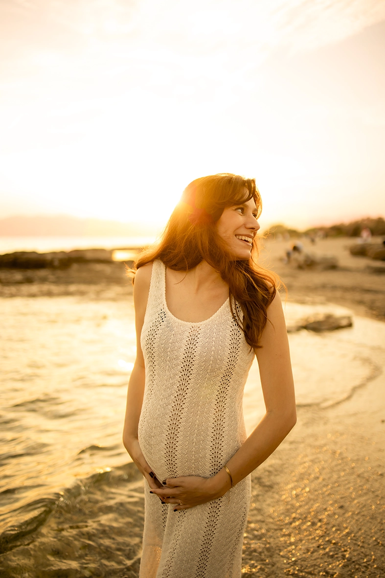 Futura mamá sonriendo al atardecer junto al mar en Mallorca.