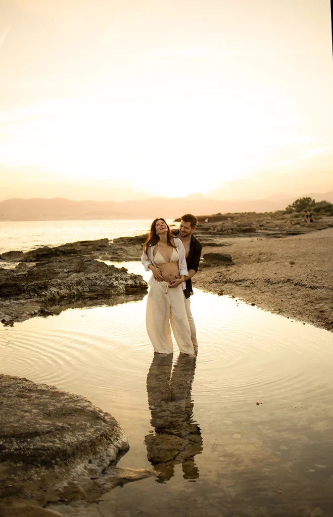Pareja embarazada riendo al atardecer junto al mar en Mallorca.