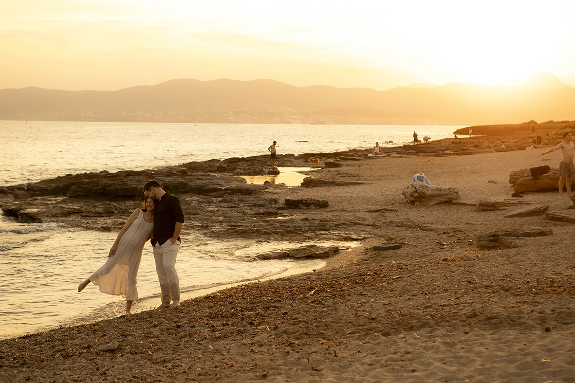 Pareja embarazada caminando junto al mar al atardecer en Mallorca.