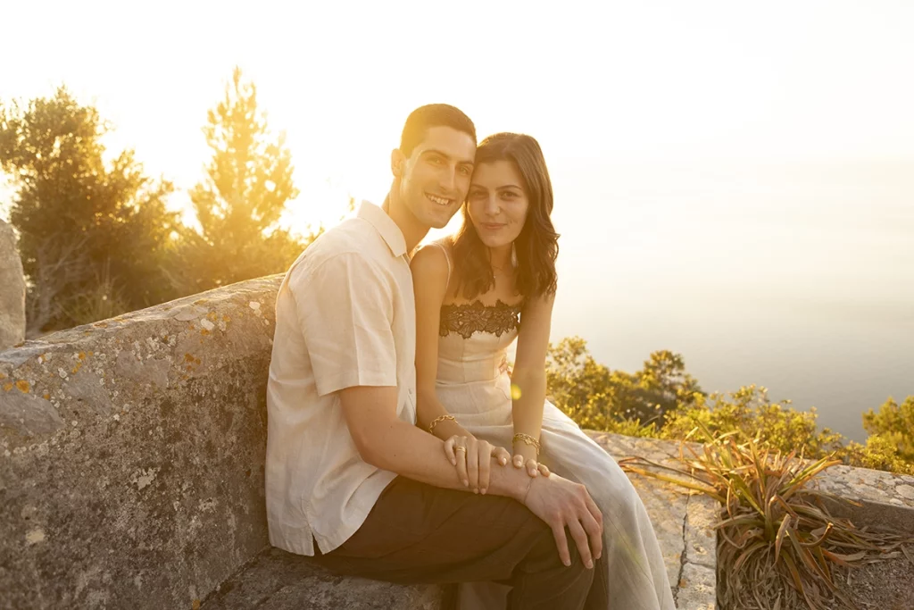 Pareja comprometida sentada al atardecer durante una fotografía para pedida en Mallorca