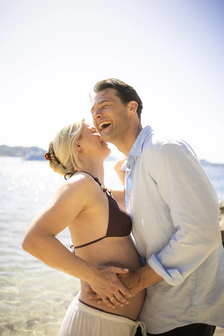Pareja embarazada riendo junto al mar en Cala Fornells.