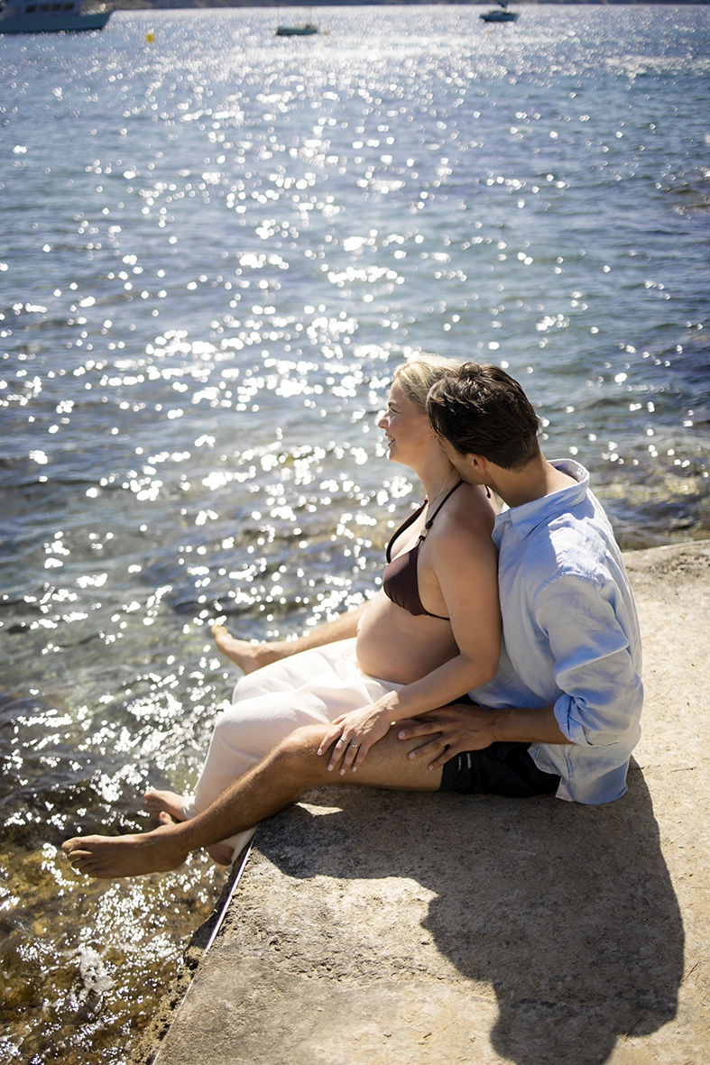 Pareja embarazada sentada junto al mar en Cala Fornells.