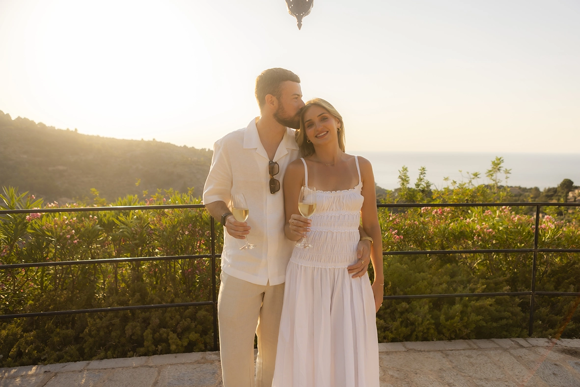 Pareja brindando tras una pedida de mano en Belmond La Residencia con vistas al Mediterráneo durante la puesta de sol.