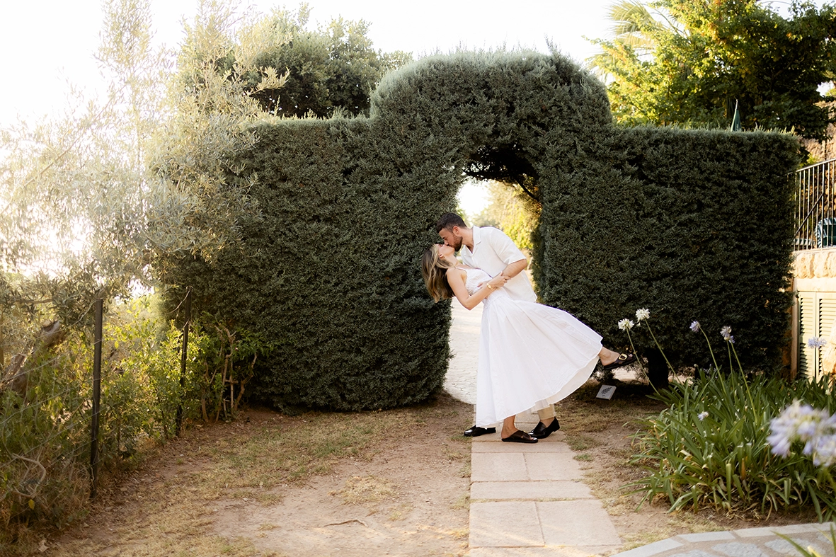besándose bajo un arco de cipreses después de su pedida de matrimonio en Belmond La Residencia, Mallorca.