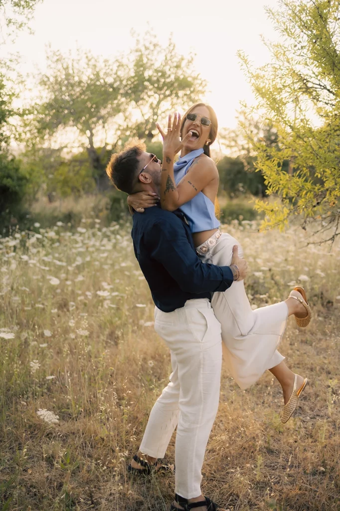 Anto y Biel riendo mientras él la levanta en una sesión de preboda al atardecer en Mallorca.