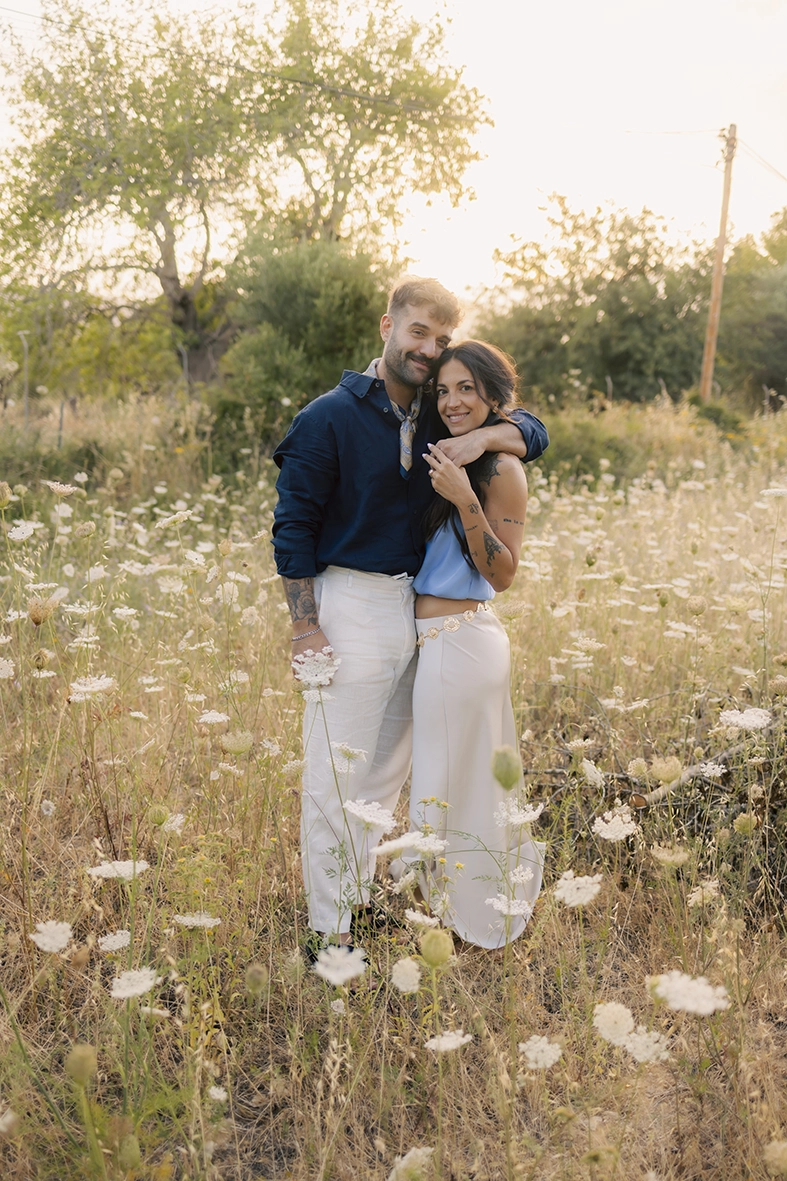 Anto y Biel abrazados entre flores silvestres durante una sesión de preboda al atardecer.