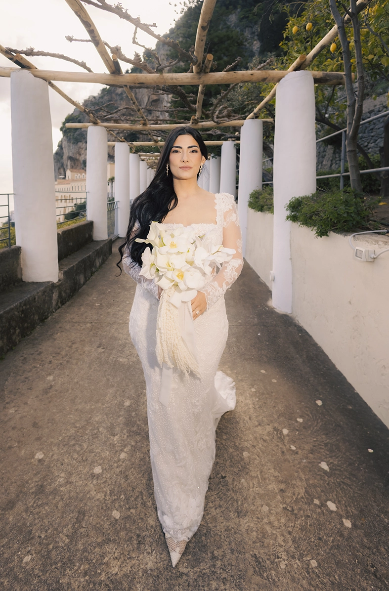 Bride holding a white orchid bouquet beneath a lemon pergola, photographed by a wedding photographer on the Amalfi Coast.