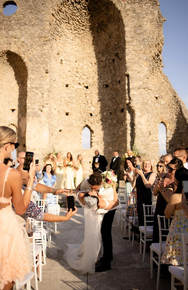 Newlyweds sharing their first kiss while guests celebrate after their wedding ceremony in Scala.