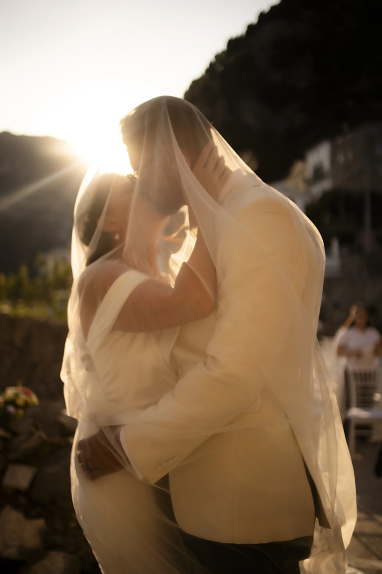 Newlyweds sharing an intimate kiss beneath the bride’s veil in the golden sunset light on the Amalfi Coast.