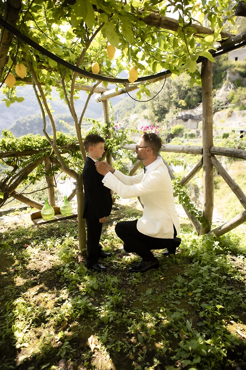Groom adjusting a young wedding guest’s bow tie beneath the lemon trees before an Amalfi Coast wedding.