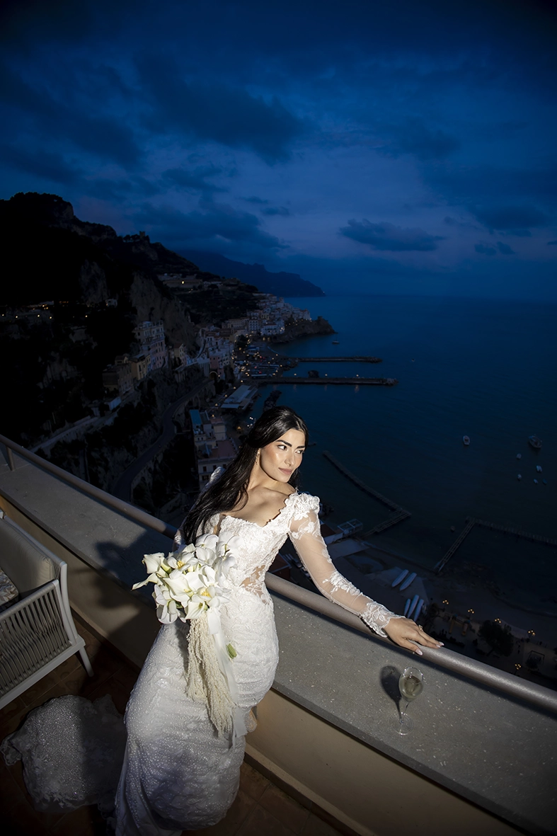 Bride holding a white orchid bouquet on a terrace overlooking Amalfi and the Mediterranean Sea.